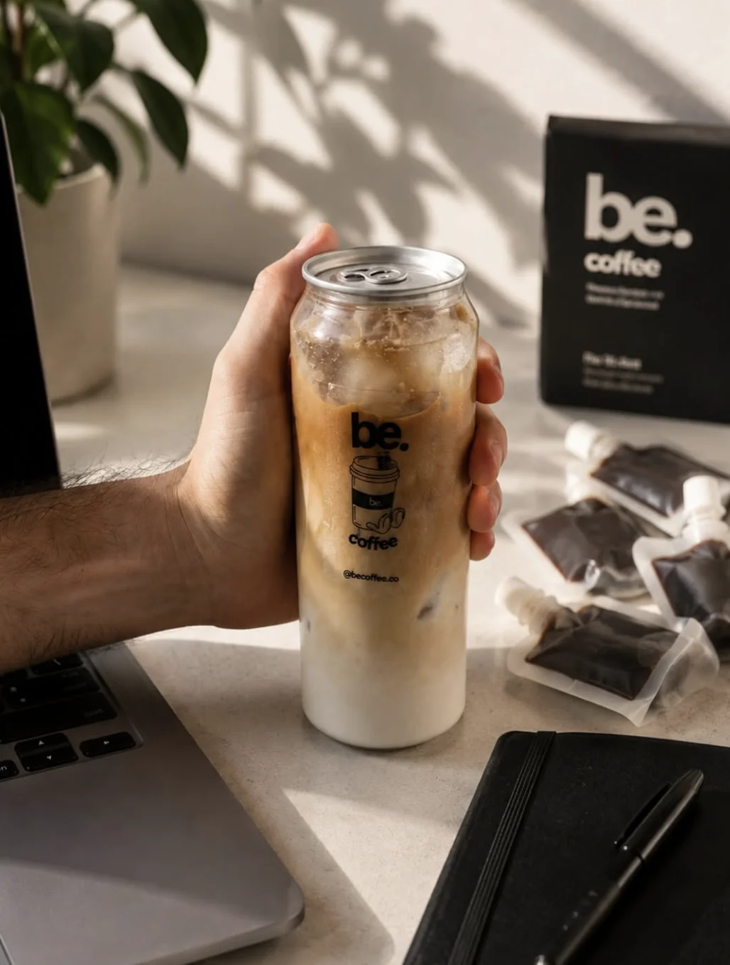 iced latte be. coffee ready to drink en la mano, junto a un portátil